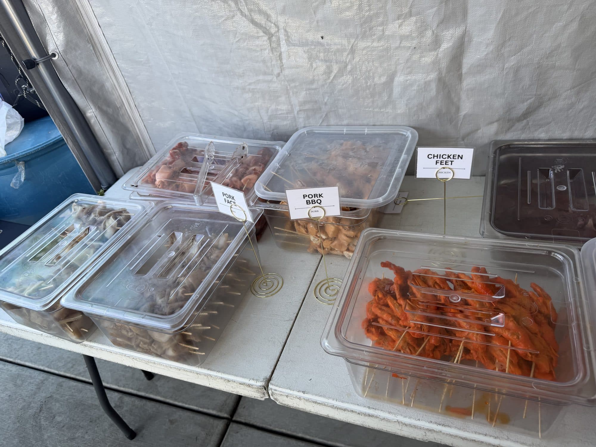 Trays of raw skewers labeled pork face, pork BBQ, and chicken feet, ready to be picked