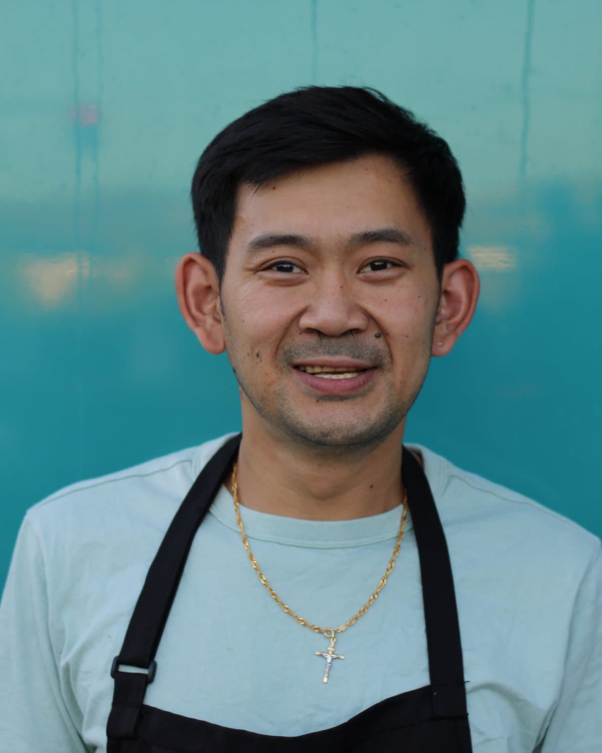 Tino, the cook and owner, smiling in his apron in front of the teal trailer